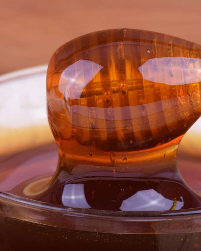 Bildaussschnitt ein typischer Holzhoniglöffel umschlossen von Honig direkt aus dem Honig in einem Glas gehoben.