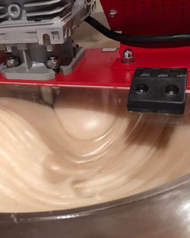 ein Bildausschnitt einer Maschine zum Honigschleudern ähnlich einer Küchenmaschine. Die Schüssel ist mit cremigem Honig gefüllt. 