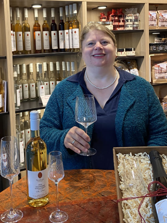 Andrea König im WasRegionales Shop in Shop im KÖNIG Plus Ladengeschäft. Sie hält ein Rippstielglas in der Hand.