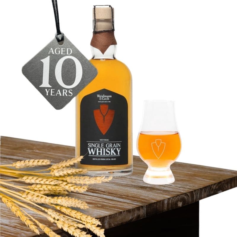 eine Flasche 10jaehrgier Single Grain Wetterau Whisky und Anhaenger 10 Jahre alt von Weidmann und Groh amit Nosingglas und Gerstenaehre auf Holztisch 